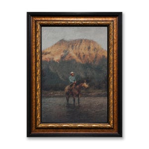 以下が含まれることがあります： 額縁に入った絵画は、川の中で馬に乗ったカウボーイと、背景に山を描いています。 このアートワークは、黒と金の装飾的なフレームに収められており、素朴なシーンにエレガンスを添えています。 この絵は、アメリカ西部の雰囲気を醸し出しています。