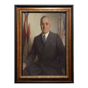 May include: A framed portrait of a man in a dark suit, white shirt, and blue tie. The portrait is set against a backdrop of the American flag and a second flag. The frame is ornate with gold and brown detailing.