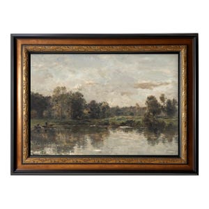 May include: An antique landscape painting in a decorative, ornate, dark brown wooden frame. The artwork depicts a serene river scene with trees, a cloudy sky, and reflections in the water. The frame has a gold-colored inner edge.