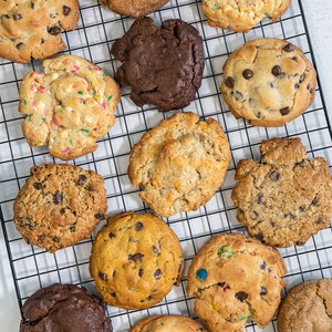 May include: A variety of cookies on a black wire rack. The cookies are a mix of chocolate chip, oatmeal raisin, sugar, and sprinkle cookies.
