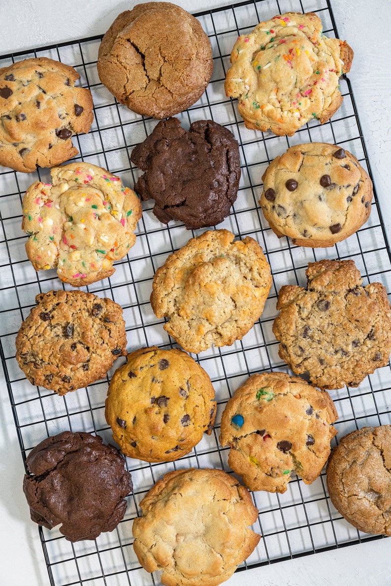 May include: A variety of cookies on a black wire rack. The cookies are a mix of chocolate chip, oatmeal raisin, sugar, and sprinkle cookies.