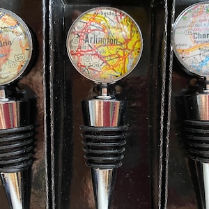 Pode incluir: Conjunto de três rolhas de garrafa com designs de mapas. Cada rolha apresenta uma cidade diferente: Alexandria, Arlington e Charleston. As rolhas têm uma base prateada e uma vedação de borracha preta. Os mapas são de forma circular.