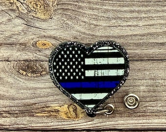 May include: A black glitter heart-shaped badge holder with a thin blue line and an American flag design. The badge holder has a retractable reel.