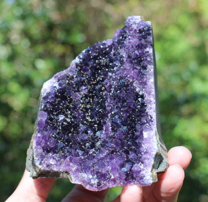 May include: A large amethyst geode with a deep purple color and a natural, rough exterior. The geode is filled with small, sparkling crystals.