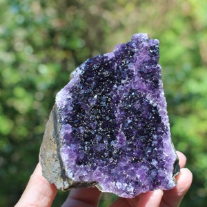 May include: A large amethyst geode with a deep purple color and a natural, rough exterior. The geode is filled with small, sparkling crystals.