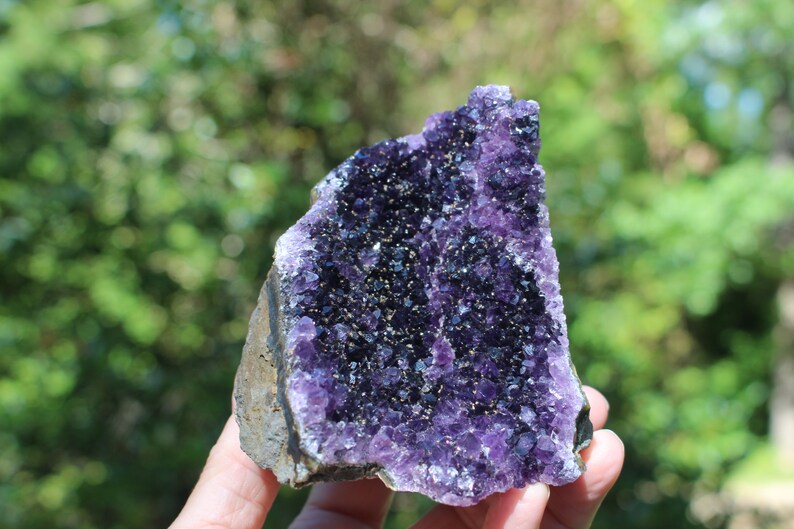 May include: A large amethyst geode with a deep purple color and a natural, rough exterior. The geode is filled with small, sparkling crystals.