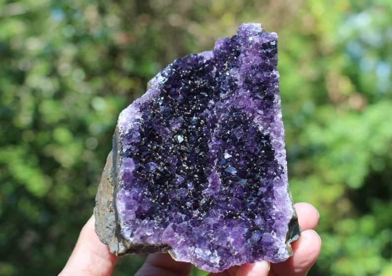 May include: A large amethyst geode with a purple and dark purple crystal formation. The geode is sitting on a hand.