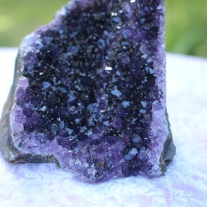 May include: A large amethyst geode with a deep purple color and a natural, rough exterior. The geode is filled with many small, sparkling crystals.