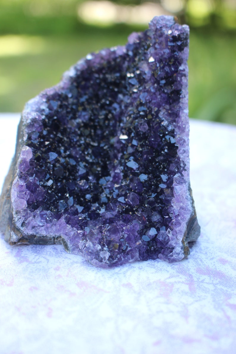 May include: A large amethyst geode with a deep purple color and a natural, rough exterior. The geode is filled with many small, sparkling crystals.