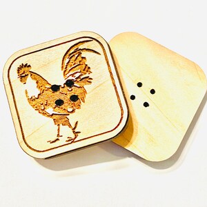 May include: A wooden salt and pepper shaker set with a rooster design. The salt shaker has a rooster engraved on the front and the pepper shaker has a plain front.