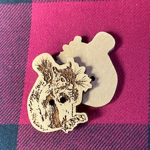 May include: A wooden button with a laser-etched image of a squirrel. The button is brown and has a hole in the center.