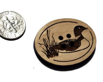 May include: A wooden button with a black and white image of a loon in a lake setting. The button is approximately 1 inch in diameter.