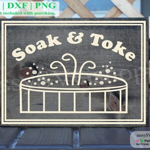 Könnte beinhalten: Ein Holzschild mit weißem Rand und dem Text "Soak & Toke" in weißer Schrift. Das Schild zeigt einen weißen Umriss eines Whirlpools mit Blasen und Dampf, der aus dem Wasser steigt.