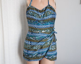 May include: A vintage swimsuit with a blue and green geometric pattern. The swimsuit has a halter top and a wrap skirt.