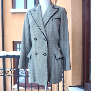 May include: A monochrome houndstooth blazer with black detailing and buttons. The jacket features a double-breasted design, two front pockets, and a chest pocket. The blazer is displayed on a mannequin.