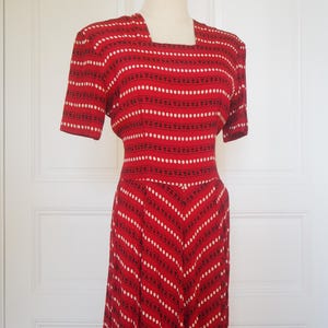 May include: A vintage red dress with a square neckline and short sleeves. The dress features a pattern of white dots and black dashes arranged in horizontal and diagonal stripes. The dress is displayed on a mannequin.