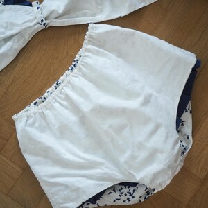 May include: White and navy blue two-piece swimsuit set. The top features a bow detail, and the bottoms are high-waisted. The navy blue fabric has a white geometric pattern. The swimsuit is made of a lightweight fabric.