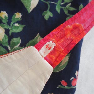 May include: Close-up of fabric with a floral pattern in navy blue, green, and yellow. A bright pink strap with orange accents is visible, along with a white fabric edge. The strap has a small, faded text.