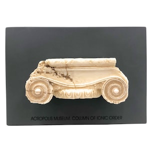 Peut inclure: Un gros plan d'un moulage en plâtre blanc d'un chapiteau de colonne ionique. Le chapiteau est monté sur un fond noir. Le texte "ACROPOLIS MUSEUM. COLUMN OF IONIC ORDER" est imprimé sous le chapiteau.