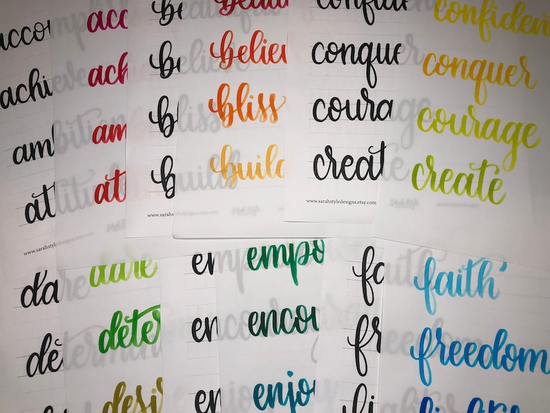 May include: A set of 10 cards with hand-lettered words in various colors, including red, orange, yellow, green, blue, and black. The words are: "accomplish", "achieve", "ambition", "attitude", "believe", "bliss", "build", "conquer", "courage", "create", "dare", "determine", "desire", "empower", "encourage", "enjoy", "faith", "freedom", "give", "grow", "happy", "heal", "hope", "inspire", "joy", "kindness", "love", "magic", "miracle", "motivate", "peace", "positive", "powerful", "pray", "purpose", "resilience", "smile", "strength", "thankful", "trust", "understand", "wisdom", "worthy", "you".