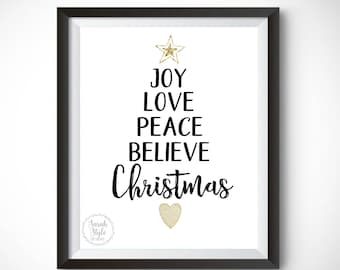 Peut inclure: Une impression encadrée en noir avec un fond blanc et une étoile dorée en haut. L'impression présente les mots "Joie, Amour, Paix, Croire, Noël" en texte noir disposés en forme de sapin de Noël. Un cœur doré se trouve au bas de l'arbre.