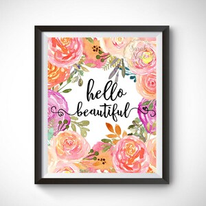 May include: A printable wall art design featuring a floral wreath with pink, orange, and white flowers. The text "hello beautiful" is written in black cursive script in the center of the wreath.