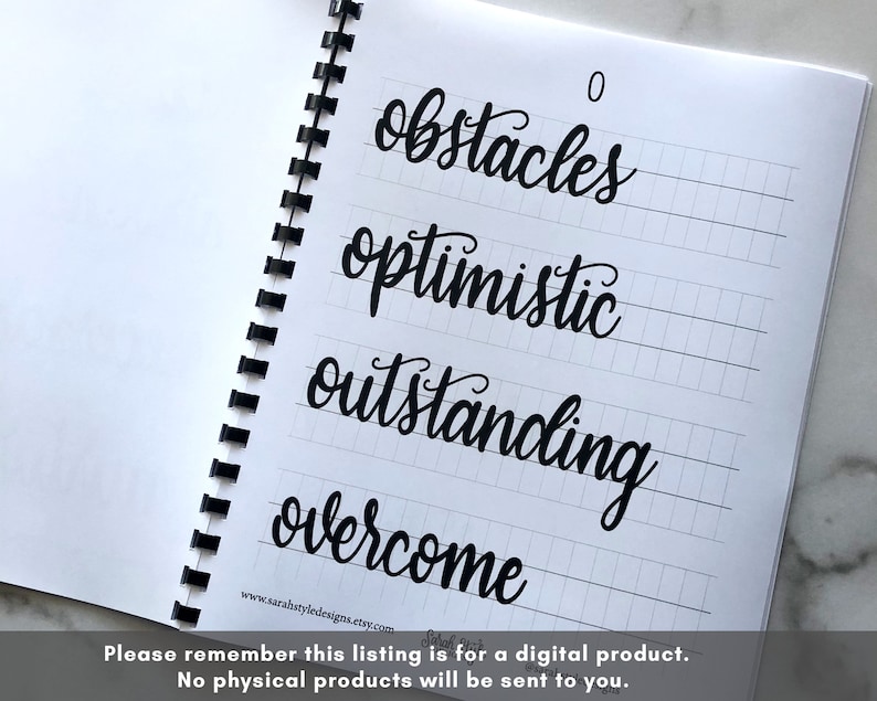 May include: A notebook with a spiral binding and lined pages. The notebook has a black ink inscription of the words "obstacles", "optimistic", "outstanding", and "overcome" on the pages. The words are written in a cursive font.