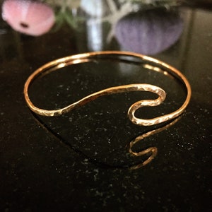 May include: A gold-toned hammered metal bracelet with a wave design. The bracelet is open and adjustable.