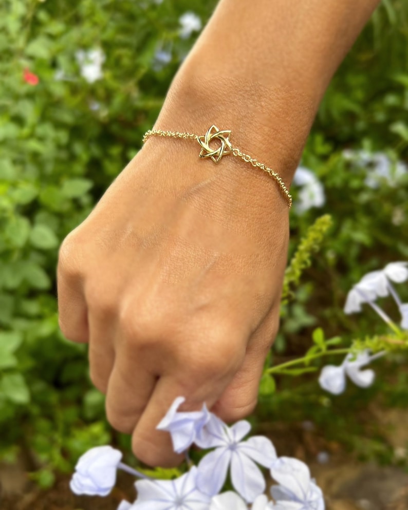K&ouml;nnte beinhalten: Ein goldenes Kettenarmband mit einem sternf&ouml;rmigen Anh&auml;nger. Das Armband befindet sich an einem Handgelenk.