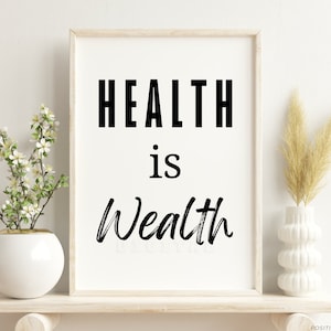 May include: A framed print with the text "HEALTH is Wealth" in black and white on a white background. The print is displayed on a shelf with a vase of white flowers and a vase of dried grass.
