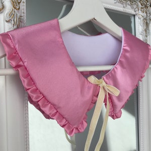 May include: A pink satin collar with a ruffled edge and a yellow satin ribbon tied in a bow.