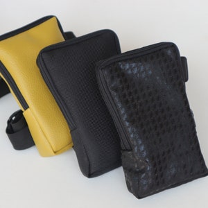 May include: Three different phone cases. One is yellow leather, one is black with a textured fabric, and the other is black with a patterned fabric.