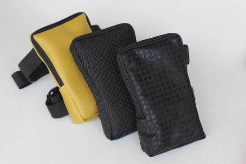 May include: Three different phone cases. One is yellow leather, one is black with a textured fabric, and the other is black with a patterned fabric.