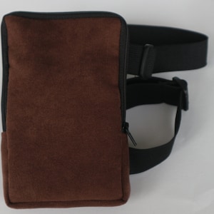May include: A brown suede phone pouch with a black zipper and a black adjustable strap.