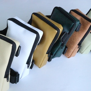 May include: A row of six small, zippered bags in various colors, including beige, white, mustard yellow, dark green, brown, and light green. Each bag has a black adjustable strap.