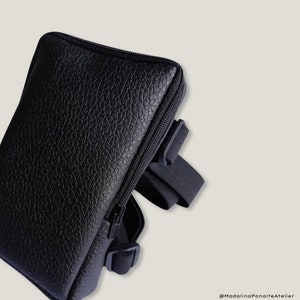 May include: A black leather phone case with a zipper closure and an adjustable strap. The case has a textured surface and is designed to be worn on the hip.