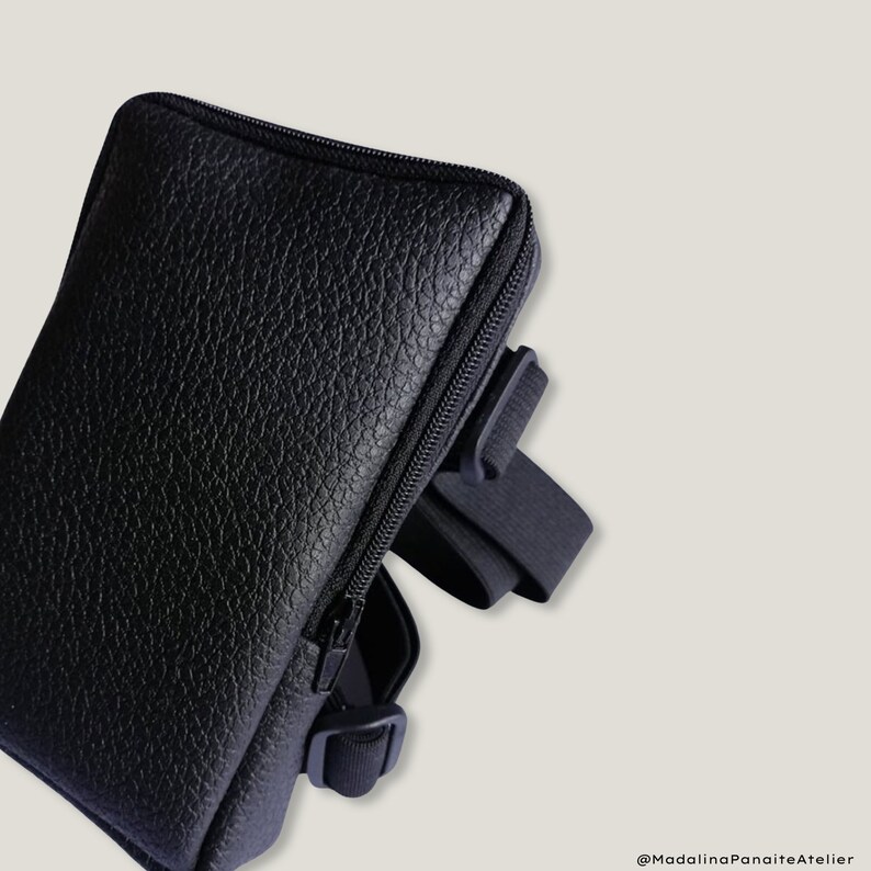 May include: A black leather phone case with a zipper closure and an adjustable strap. The case has a textured surface and is designed to be worn on the hip.