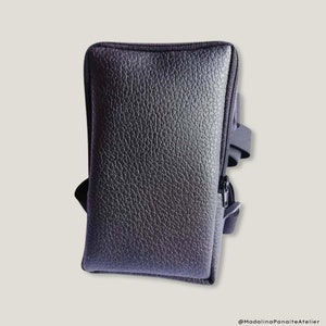 May include: A black leather phone case with a zipper closure and a strap. The case has a textured surface and a zipper pull with a black strap.