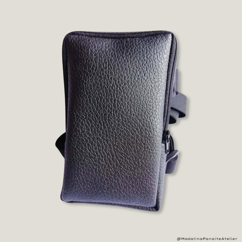 May include: A black leather phone case with a zipper closure and a strap. The case has a textured surface and a zipper pull with a black strap.