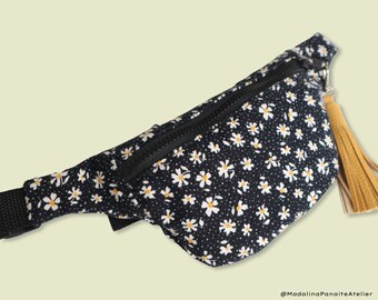 May include: A black fanny pack with a white daisy print and a black zipper. The fanny pack has a yellow tassel.