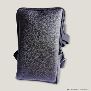 May include: Black leather phone case with a zipper closure and a strap for carrying. The case has a textured surface.
