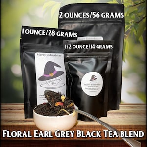 May include: Three black bags of loose leaf tea with a witch's hat logo and the text "Merry Unbirthday!"  The bags are labeled with different weights: 2 ounces/56 grams, 1 ounce/28 grams, and 1/2 ounce/14 grams. The tea is a floral earl grey black tea blend.