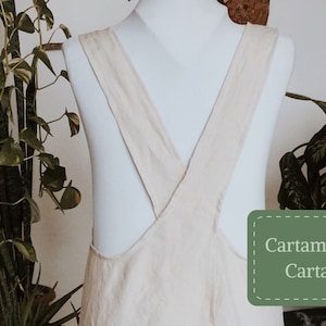 Op de afbeelding: Een beige linnen schort met gekruiste banden op de rug. Het schort heeft een label met de tekst "Cartam modello Cartaceo" met een schaar.