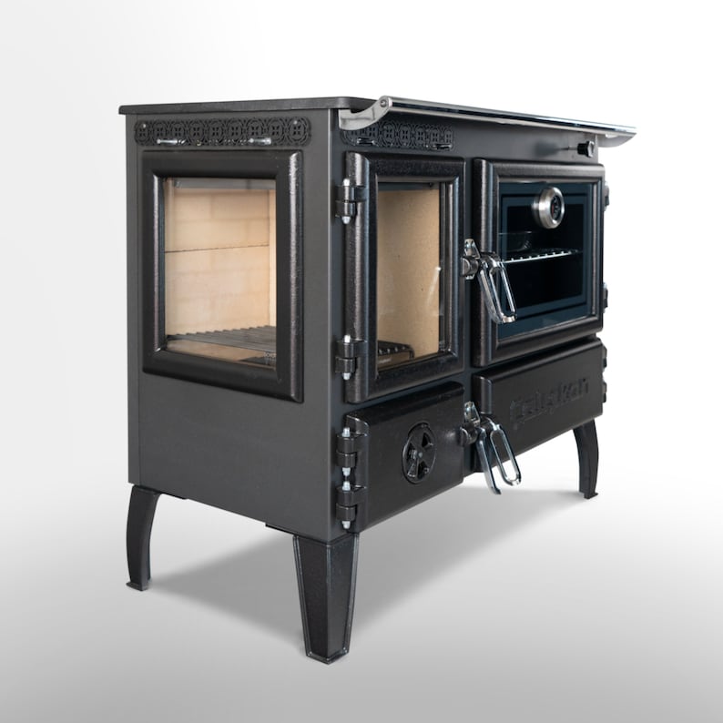 May include: Black cast iron wood-burning stove with a glass door and a side oven. The stove has a decorative design on the top and sides. The stove is on four legs.