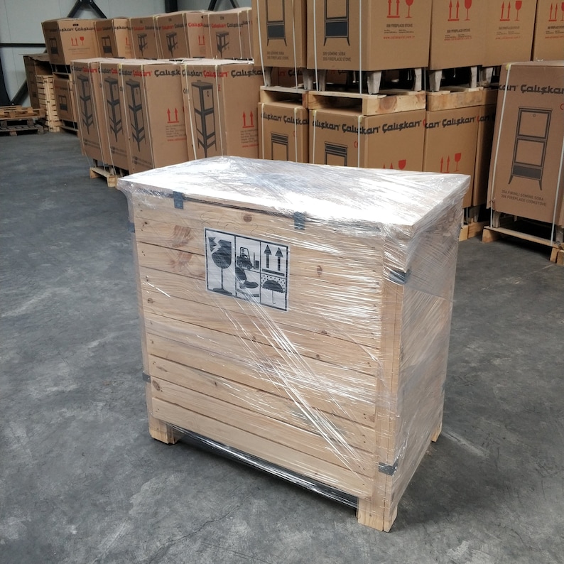 May include: A wooden crate with a clear plastic wrap, secured with black straps. The crate has a label with a symbol indicating fragile contents and arrows indicating the direction to lift the crate.