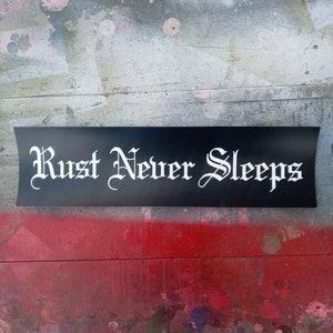 Puede incluir: Pegatina negra y blanca con el texto "Rust Never Sleeps" en una fuente gótica.