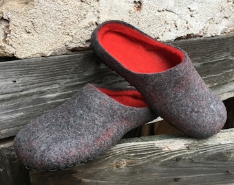 May include: A pair of gray felt slippers with red felt lining. The slippers are sitting on a wooden surface.
