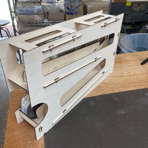 May include: A wooden toy with a ramp and a storage compartment. The toy is made of light wood and has a natural finish. It is designed to hold small objects, such as marbles or toy cars.