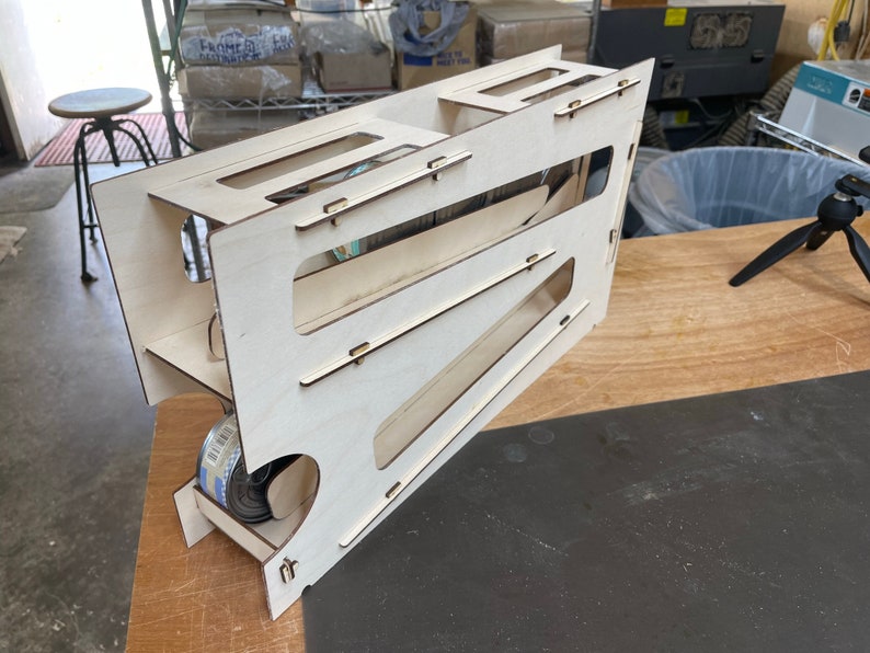 May include: A wooden toy with a ramp and a storage compartment. The toy is made of light wood and has a natural finish. It is designed to hold small objects, such as marbles or toy cars.