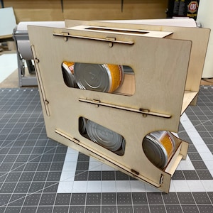 May include: A wooden storage rack with multiple shelves for holding canned goods. The rack is made of light brown wood and has a natural finish. The shelves are angled to create a cascading effect, allowing for easy access to the cans.